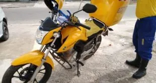 Motociclista de capacete amarelo ao lado de moto com baú de entregas na rua