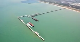 Vista aérea de píer de porto avançando sobre o mar esverdeado com navios atracados