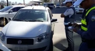 Agentes de trânsito de colete abordam carro branco parado em avenida à beira-mar