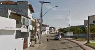 Poste de energia com fiação em rua residencial ladeada por casas e um carro ao fundo
