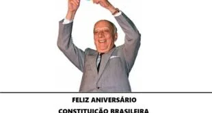Homem de terno ergue exemplar da Constituição sobre a legenda 'Feliz aniversário Constituição Brasileira 1988'
