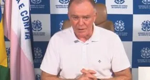 Homem de camisa branca fala diante de painel com brasões do Governo do Espírito Santo