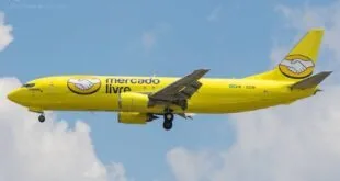 Avião amarelo com a marca Mercado Livre em voo sob céu azul com nuvens