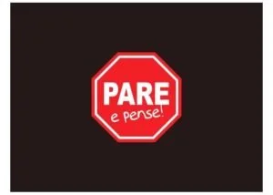 Placa vermelha de pare com os dizeres 'Pare e pense!' sobre fundo escuro