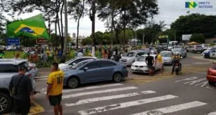 Manifestantes com bandeiras do Brasil e roupas verde-amarelas em avenida com carros parados