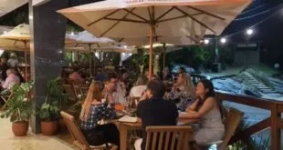 Pessoas sentadas em mesas de restaurante ao ar livre à noite sob guarda-sol iluminado