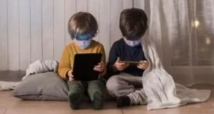 Dois meninos sentados lado a lado usando tablet e celular, com a luz das telas no rosto