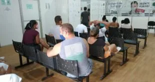 Pessoas de máscara sentadas em cadeiras de uma sala de espera de unidade de saúde