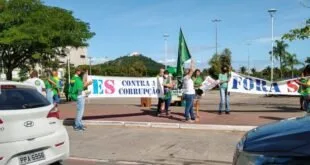 Manifestantes na rua com bandeiras do Brasil e faixa com a palavra 'corrupção' diante de morro