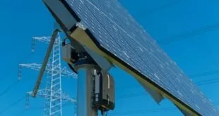 Painel solar visto de baixo com torre de transmissão de energia e céu azul ao fundo