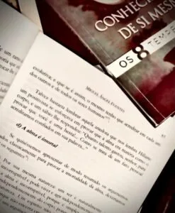 Livro aberto com páginas de texto ao lado de outro livro de capa vermelha escura