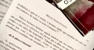 Livro aberto com páginas de texto ao lado de outro livro de capa vermelha escura