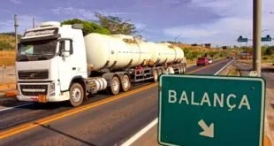 Caminhão-tanque trafegando em rodovia ao lado de placa verde de sinalização