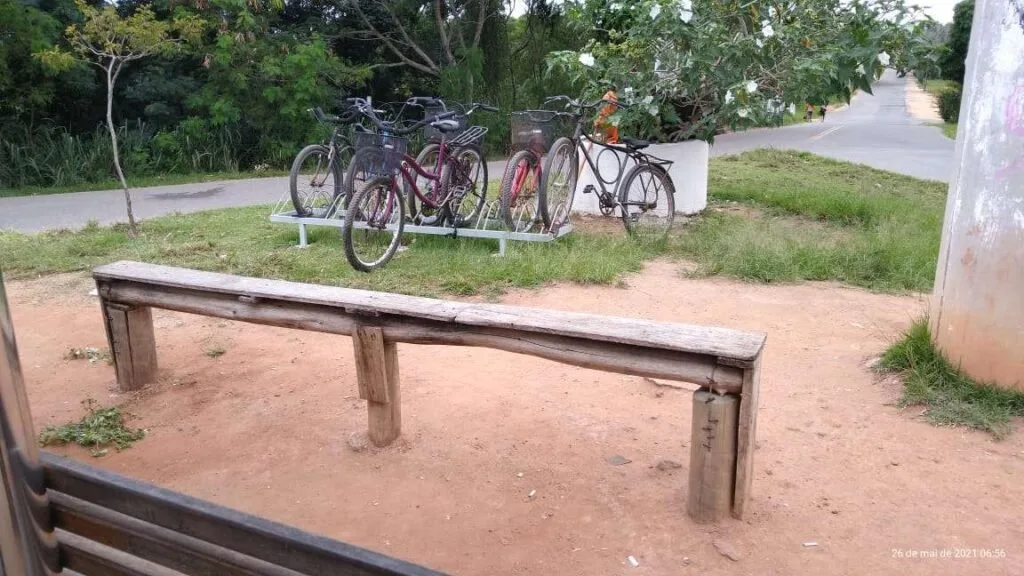 Bicicletas estacionadas em suporte de madeira ao ar livre, com banco rústico e chão de terra