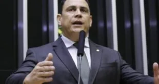 Homem de terno discursa ao microfone na tribuna de um plenário