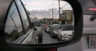 Reflexo em retrovisor de carro mostrando fila de veículos em avenida congestionada
