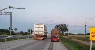 Caminhão de carga e carro vermelho trafegando em rodovia ao entardecer