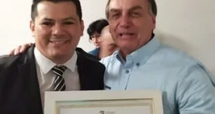 Dois homens posam juntos segurando um certificado emoldurado em ambiente interno