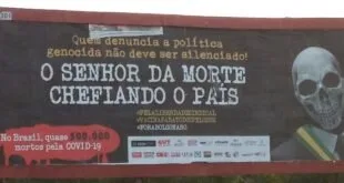 Outdoor às margens de estrada com mensagem de protesto em letras brancas sobre fundo escuro