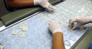 Mãos com luvas conferem preservativos alinhados em esteira de linha de produção