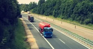 Dois caminhões trafegam em rodovia de pista dupla cercada por vegetação