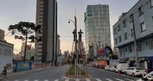 Avenida urbana com prédios altos, faixa de pedestres e relógio de rua ao amanhecer
