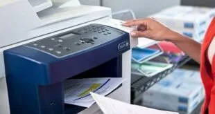 Mão aciona o painel de uma impressora multifuncional com folhas impressas na bandeja
