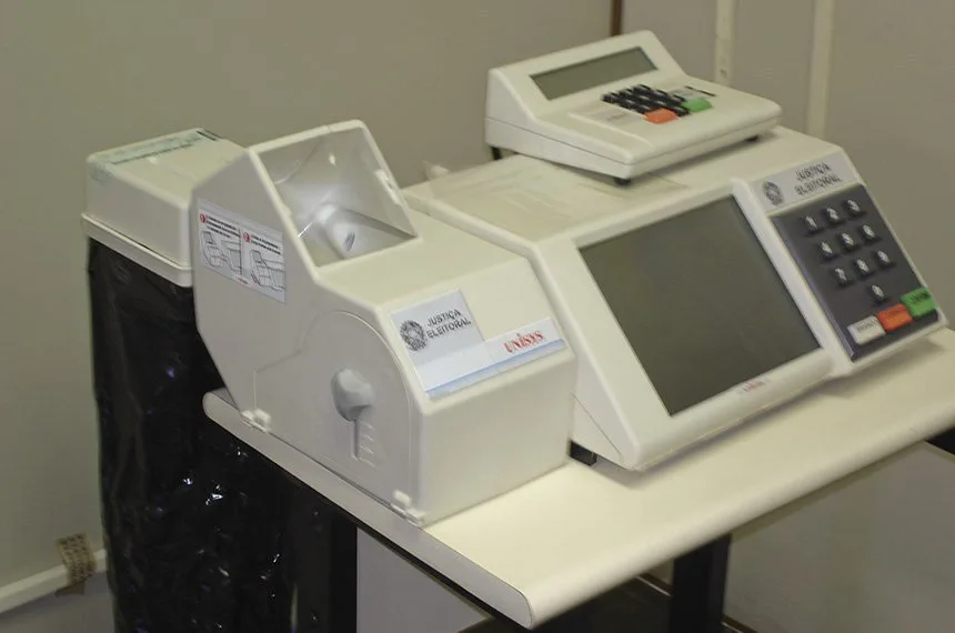 Urnas eletrônicas de votação sobre mesa em sala de ambiente interno