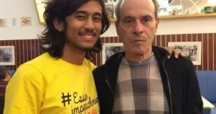 Dois homens posam lado a lado, um deles com camiseta amarela estampada
