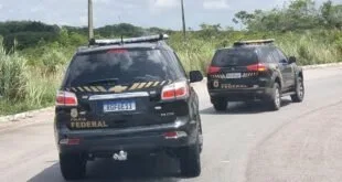 Duas viaturas da Polícia Federal trafegando em rodovia com vegetação ao redor
