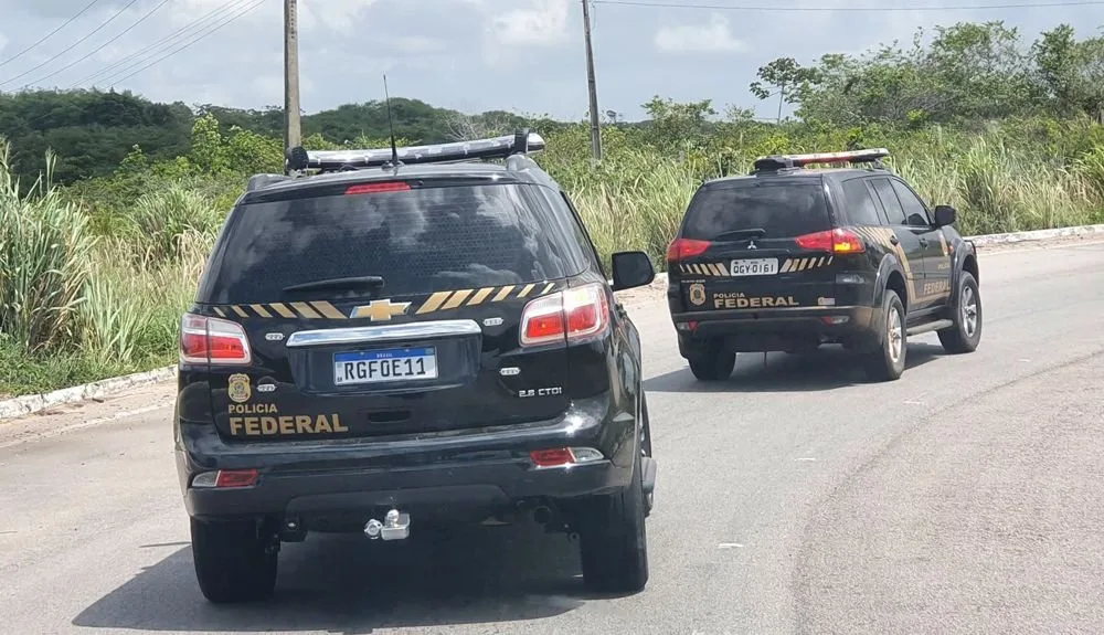 Duas viaturas da Polícia Federal trafegando em rodovia com vegetação ao redor