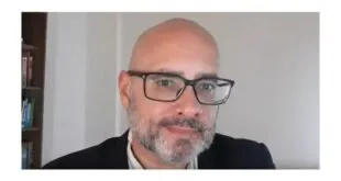 Homem careca, de barba grisalha e óculos, em retrato feito em ambiente interno