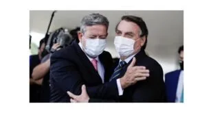 Dois homens de máscara se abraçam durante cumprimento diante de câmeras