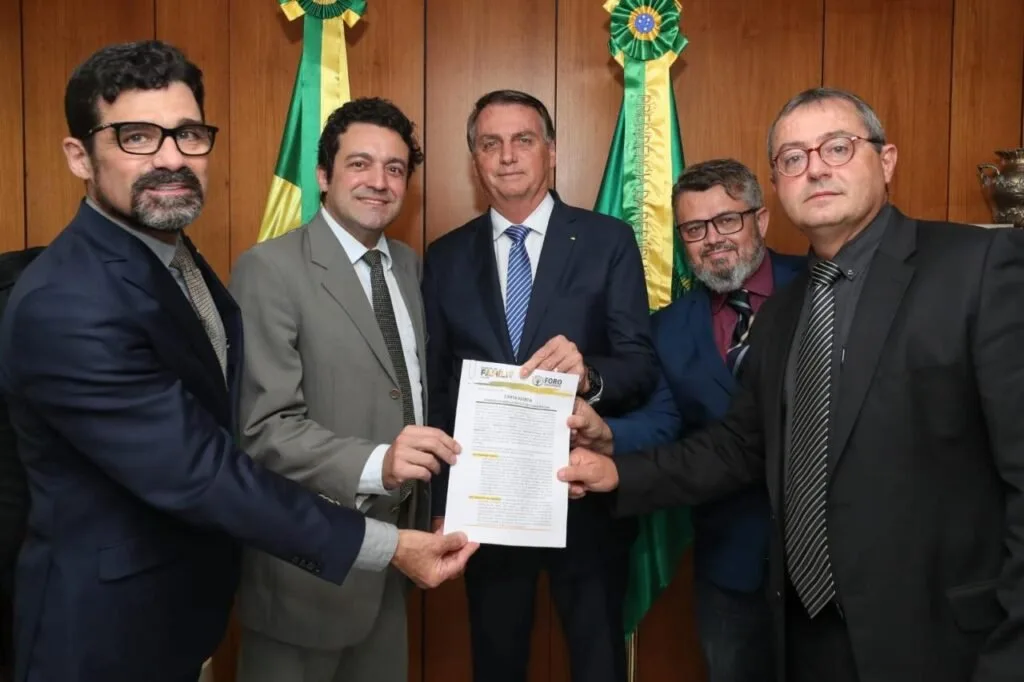 Grupo de homens de terno posa segurando um documento, com bandeiras do Brasil ao fundo
