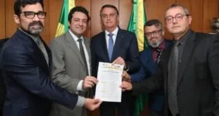 Grupo de homens de terno posa segurando um documento, com bandeiras do Brasil ao fundo