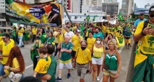 Multidão vestida de verde e amarelo em manifestação numa avenida cercada de prédios