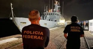 Agentes com coletes da Polícia Federal observam embarcação atracada durante a noite