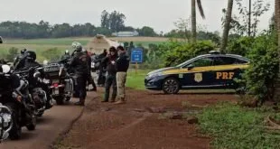 Policiais rodoviários abordam motociclistas em estrada de terra, ao lado de viatura
