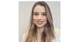 Mulher jovem de jaleco branco sorri em retrato com fundo claro
