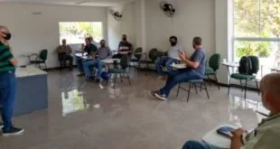 Pessoas sentadas em roda de cadeiras durante reunião em sala com ventiladores de parede