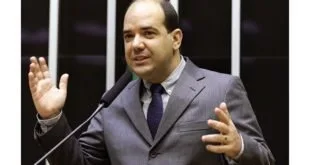 Homem de terno gesticula ao falar em tribuna de plenário com microfones à frente