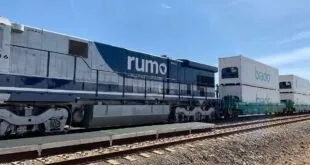 Locomotiva com a marca 'rumo' parada sobre trilhos em pátio ferroviário