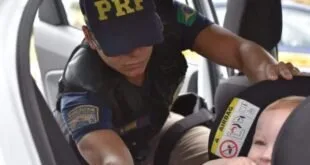 Agente da PRF ajusta uma criança na cadeirinha no banco de um carro