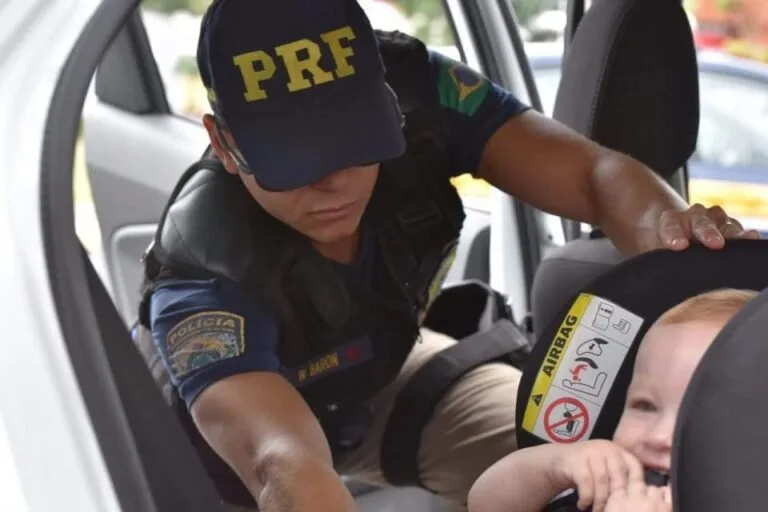 Agente da PRF ajusta uma criança na cadeirinha no banco de um carro