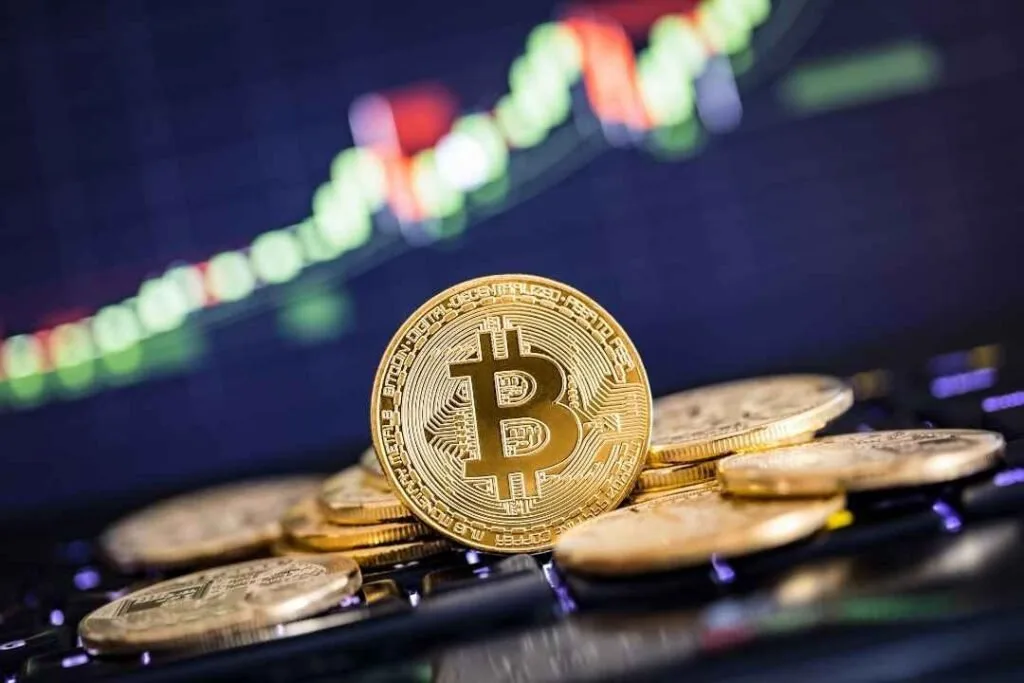 Moeda dourada de bitcoin sobre outras moedas, com gráfico de cotações desfocado ao fundo