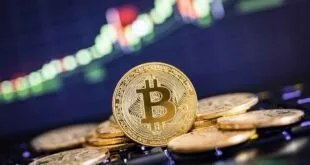 Moeda dourada de bitcoin sobre outras moedas, com gráfico de cotações desfocado ao fundo