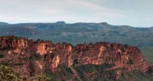 Paredões rochosos avermelhados cercados de vegetação em paisagem de chapada