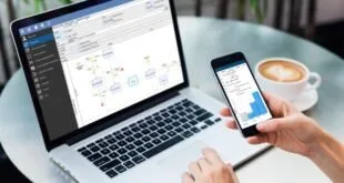 Notebook com fluxograma na tela e mão segurando celular sobre mesa de trabalho