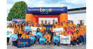 Funcionários de camiseta laranja e azul posam diante de um portal inflável da Loga