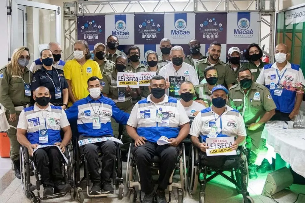 Grupo posa para foto em evento, com pessoas em cadeiras de rodas segurando placas
